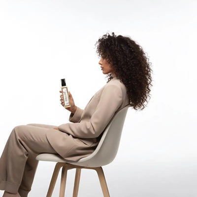 Una bottiglia elegante e rettangolare con tappo nero ed etichetta dorata tenuta in mano.