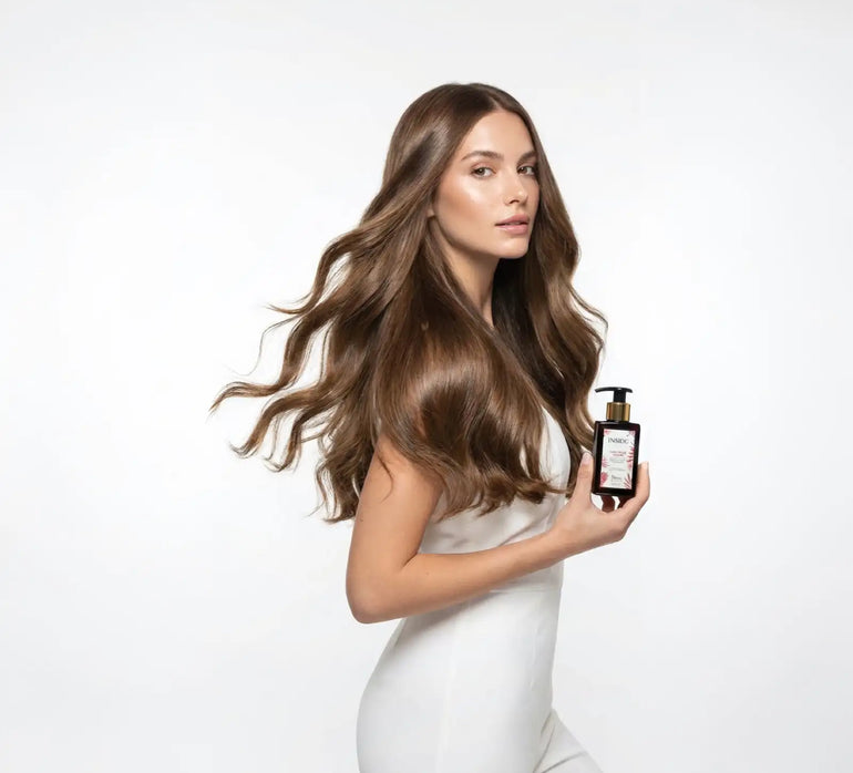 Bottiglia di vetro ambrato scuro con dispensatore a pompa dorato e un'etichetta con elementi di design floreali.