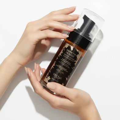 Un detergente schiumogeno elegante e color ambra in una bottiglia trasparente con pompa nera ed etichetta decorativa con foglia d'oro.