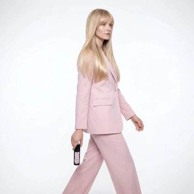 Una donna in un elegante completo rosa tenue cammina con sicurezza, tenendo una clutch nera elegante ornata con delicata ricamatura floreale bianca.