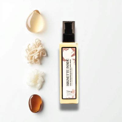 Una elegante bottiglia giallo pallido di siero per capelli per brunette con un dispensatore a pompa nero e etichetta con motivo floreale.